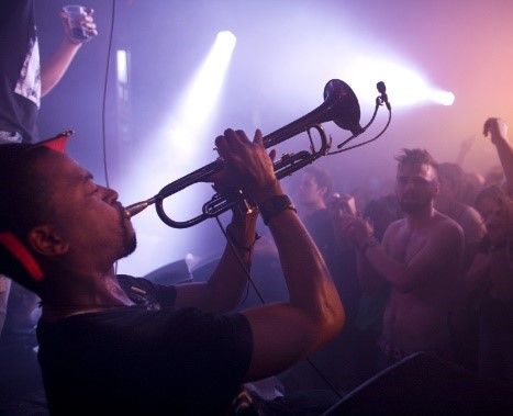 Edinburgh-Jazz-Festival. Im Vordergrund ein Trompete spielender Musiker. Hintergrund die Beifall klatschenden Zuhörer.