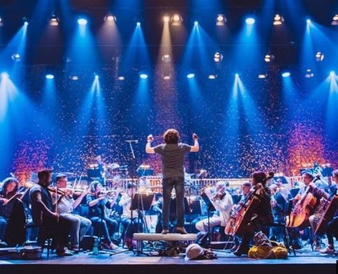Edinburgh-Theater-Festival. Dirigent stimmt Musiker ein. Im Hintergrund mit Spot-Lights aufgehellte Halle der jubelnden Fans.